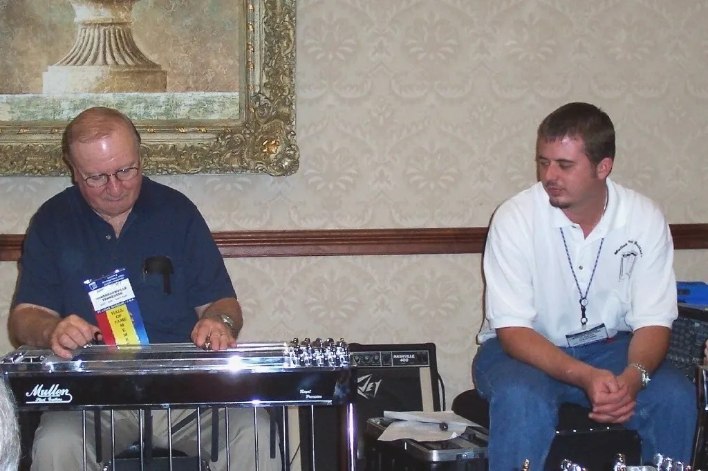 Two men sitting at a table playing a guitar.