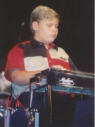 A boy in a red shirt playing a keyboard.